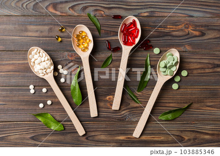 Top view Variety of vitamin and mineral pills in wooden spoon on Colored background. Top view of assorted pharmaceutical medicine pills. Dietary supplement healthcare product Top view Variety of vitamin and mineral pills in wooden spoon on Colored background. Top view of assorted pharmaceutical medicine pills. Dietary supplement healthcare product 103885346