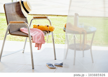 Summer patio. Chair with beach towel, striped shirt. marine flip flops and hat. Party covered by sheer curtain Exotic vacation. travel destination scenics retreat recreation with copy space. Summer patio. Chair with beach towel, striped shirt. marine flip flops and hat. Party covered by sheer curtain Exotic vacation. travel destination scenics retreat recreation with copy space. 103885926