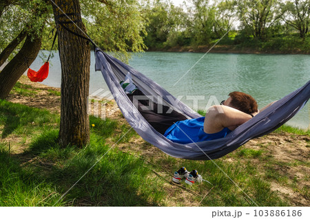 A young man rests in a hammock on the river bank 103886186