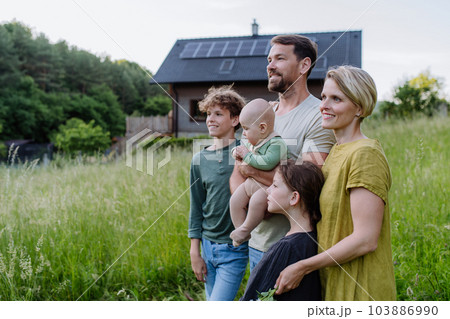 Happy family near their house with solar panels. Alternative energy, saving resources and sustainable lifestyle concept. 103886990