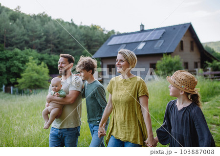 Happy family near their house with solar panels. Alternative energy, saving resources and sustainable lifestyle concept. Happy family near their house with solar panels. Alternative energy, saving resources and sustainable lifestyle concept. 103887008