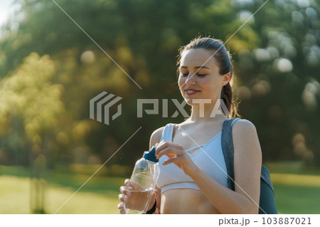 Medium shot of athletic girl in sportswear drinking water from bottle after workout. 103887021