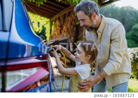 Father with his little daughter charging their electric car. Father with his little daughter charging their electric car. 103887125