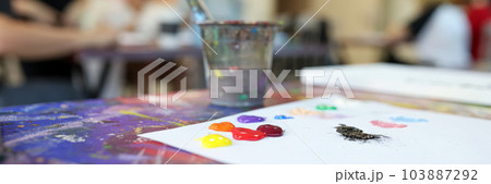 Paint brushes in glasses and colourful paints on white sheet of paper 103887292
