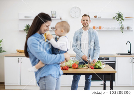 Infant treating mommy with banana while father making dinner 103889800