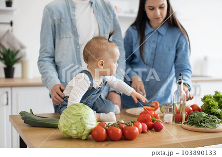 Baby on table reaching out for cucumber in mom's hand 103890133