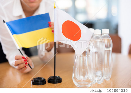 Little flag of Japan on table and flag of Ukraine put next to it by young woman 103894036