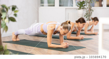 Woman performing Bhujangasana or Cobra pose during yoga class with female group in fitness studio 103894170