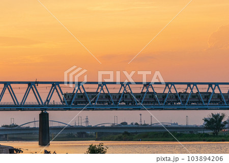 夕景に染まる空と多摩川の間を走る京王線 103894206