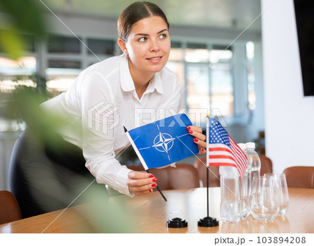 International relations meeting. Girl setting up NATO and USA flags on table 103894208