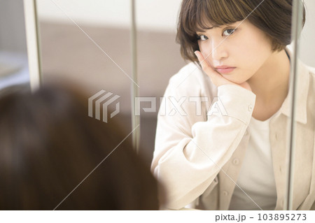 メイクをする女性の鏡越しのポートレート（悩んだ表情） 103895273
