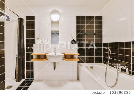 a small bathroom with black and white tiles on the walls, along with a bathtub in the foreground 103896859
