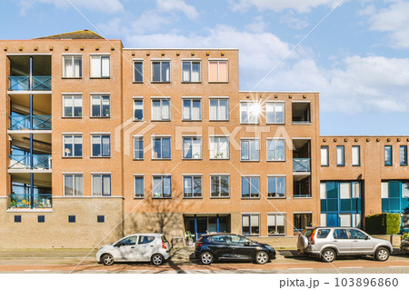 two cars parked in front of an apartment building on a sunny day with blue sky and fluffy white clouds above two cars parked in front of an apartment building on a sunny day with blue sky and fluffy white clouds above 103896860
