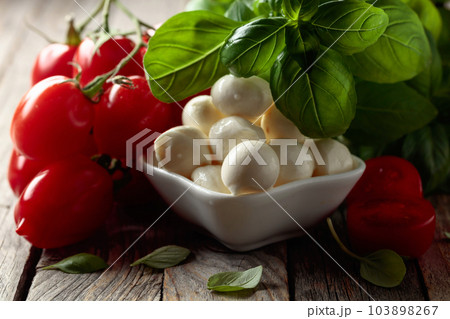 Mozzarella cheese with basil and tomatoes on an old wooden table. Mozzarella cheese with basil and tomatoes on an old wooden table. 103898267