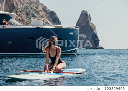 Woman sea sup. Close up portrait of happy young caucasian woman with long hair looking at camera and smiling. Cute woman portrait in bikini posing on sup board in the sea 103899466
