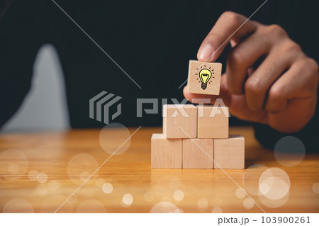 New idea and creativity concept. Wooden blocks with glowing light bulb icon on hand icon, suggesting inspiration and imagination with copy space. Designing innovative business solutions. New idea and creativity concept. Wooden blocks with glowing light bulb icon on hand icon, suggesting inspiration and imagination with copy space. Designing innovative business solutions. 103900261