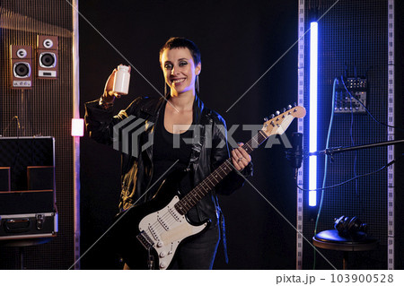 Smiling musician holding bottle of pills reviewing product in front of camera while recording new rock song using electric guitar in sound studio. Performer working at grunge album practicing songs Smiling musician holding bottle of pills reviewing product in front of camera while recording new rock song using electric guitar in sound studio. Performer working at grunge album practicing songs 103900528