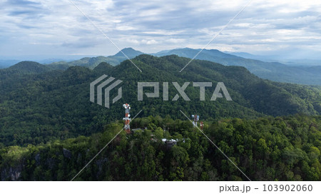 Communication tower, radio tower, telecommunication tower or transmission tower in the forest on the mountain with clouds and blue sky background. Communication tower, radio tower, telecommunication tower or transmission tower in the forest on the mountain with clouds and blue sky background. 103902060
