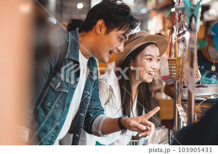 Asian couple tourist backpacker enjoying and eating street food in night market with crowd of people at Yaowarat road, Bangkok, Thailand 103905431