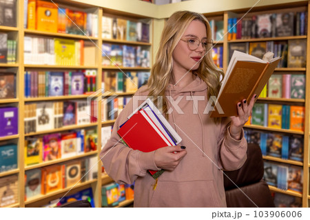 Pretty blonde woman standing with books in library Pretty blonde woman standing with books in library 103906006