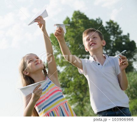 Two kids with paper planes outdoors. 103906966