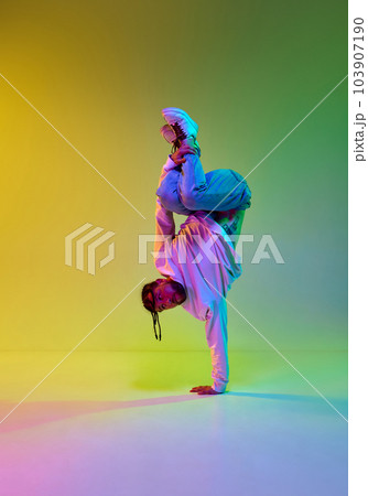 Young talented guy with dreads hairstyle dancing hip-hop, breakdance against gradient yellow green studio background in neon light Young talented guy with dreads hairstyle dancing hip-hop, breakdance against gradient yellow green studio background in neon light 103907190