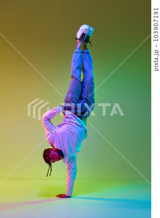 Young man with dreads hairstyle dancing hip-hop, breakdance against gradient yellow green studio background in neon light Young man with dreads hairstyle dancing hip-hop, breakdance against gradient yellow green studio background in neon light 103907191