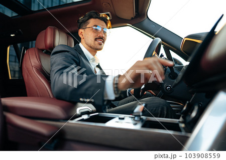 Young businessman in elegant suit driving luxury car Young businessman in elegant suit driving luxury car 103908559