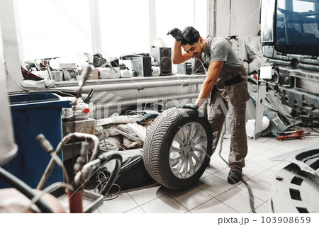 Mechanic pushing a car tire in car service Mechanic pushing a car tire in car service 103908659