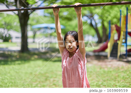 夏の公園で鉄棒を遊んでいる小学生の女の子の様子 103909559