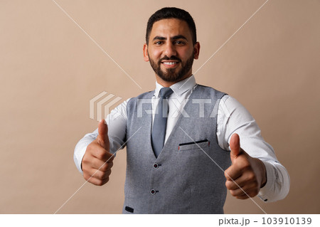 Happy young arab man showing thumbs up sign against beige background Happy young arab man showing thumbs up sign against beige background 103910139