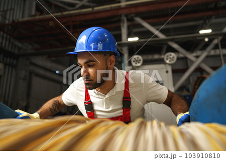 A young factory workman rolls heavy coil of electric cable 103910810
