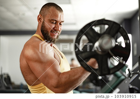 Strong bodybuilder with muscular chest and shoulders in gym Strong bodybuilder with muscular chest and shoulders in gym 103910915