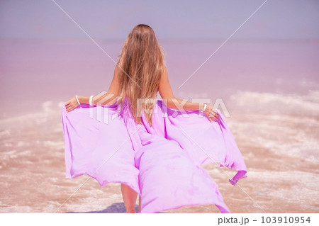 Woman pink salt lake. Against the backdrop of a pink salt lake, a woman in a long pink dress takes a leisurely stroll along the white, salty shore, capturing a wanderlust moment. Woman pink salt lake. Against the backdrop of a pink salt lake, a woman in a long pink dress takes a leisurely stroll along the white, salty shore, capturing a wanderlust moment. 103910954