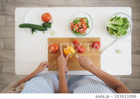 Close up of a woman and girl cutting vegetables for salad in kitchen Close up of a woman and girl cutting vegetables for salad in kitchen 103911006