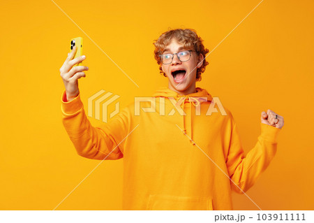 Portrait of young man playing online game on mobile phone over yellow background 103911111