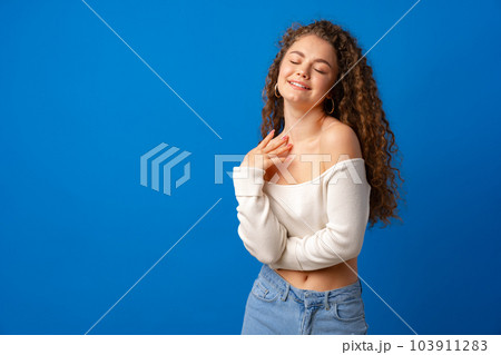 Portrait of a young attractive curly-haired woman against blue background Portrait of a young attractive curly-haired woman against blue background 103911283