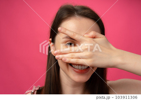 Young woman smiling and covering her face with hand, studio portrait 103911306