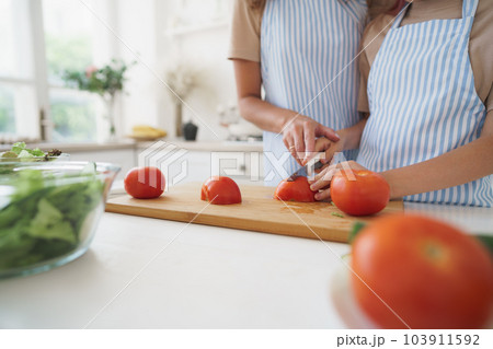 Close up of a woman and girl cutting vegetables for salad in kitchen Close up of a woman and girl cutting vegetables for salad in kitchen 103911592