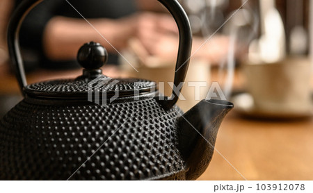 Black metal teapot with hot tea at the kitchen. Tea drinking traditions. Girl making a tea. 103912078