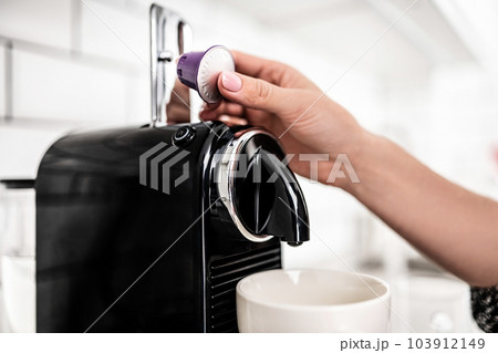 Girl hand put capsule to coffee machine at home closeup. Woman preparing italian caffeine beverage using professional espresso maker Girl hand put capsule to coffee machine at home closeup. Woman preparing italian caffeine beverage using professional espresso maker 103912149