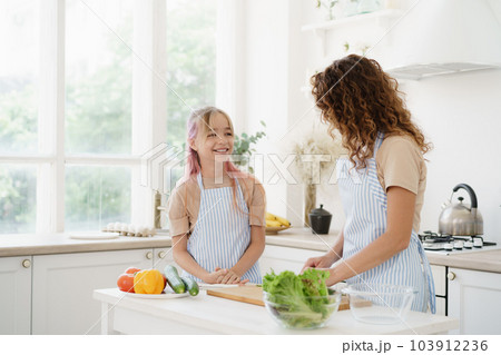 Mother and teen daughter preparing vegetable salad at kitchen 103912236
