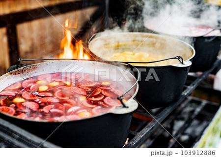 Beverages fruits and berries hot mulled wine in pots with steam in street food market. Colorful hot sweet drinks at fair festival outdoors closeup Beverages fruits and berries hot mulled wine in pots with steam in street food market. Colorful hot sweet drinks at fair festival outdoors closeup 103912886
