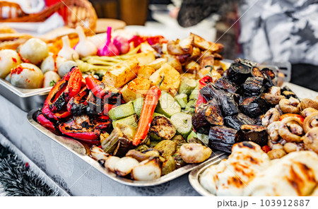 Variety of grilled vegetables as eggplant, zucchini and garlic at street food market. Traditional fried veggies at outdoor fair Variety of grilled vegetables as eggplant, zucchini and garlic at street food market. Traditional fried veggies at outdoor fair 103912887