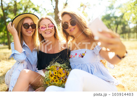 Three nice girls having fun In the park and make selfie. Excellent sunny weather. Beautiful figures. 103914403