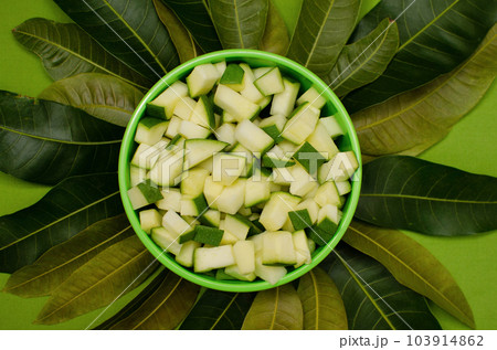 Raw mango pieces in Green bowl with mango tree leaves on Green background 103914862