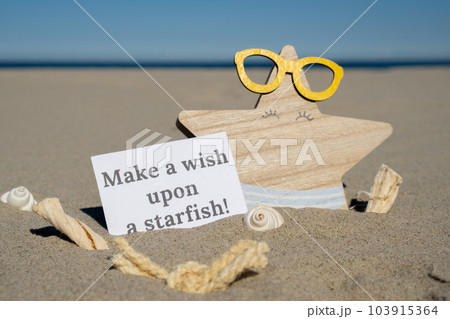 MAKE A WISH UPON A STARFISH text on paper greeting card on background of funny starfish in glasses summer vacation decor. Sandy beach sun coast. Holiday concept postcard. Getting away Travel 103915364