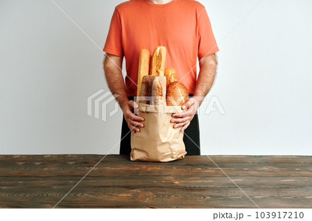 Man holds fresh loaves of bread baguettes in paper bag over light background 103917210