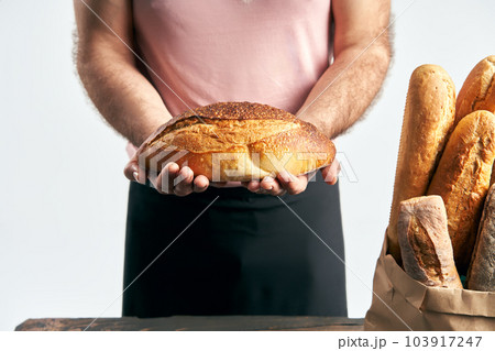 Baker man in apron holding loaf of fresh baked bread in the hands 103917247