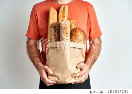 Man holds fresh loaves of bread baguettes in paper bag over light background Man holds fresh loaves of bread baguettes in paper bag over light background 103917255